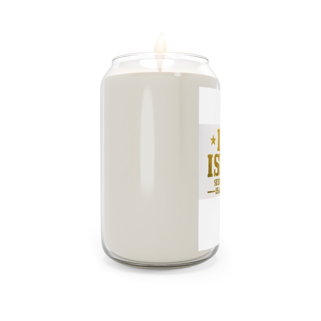 A lit candle in a clear glass jar with a white wax body and a white label gold text , shown against a plain white background 