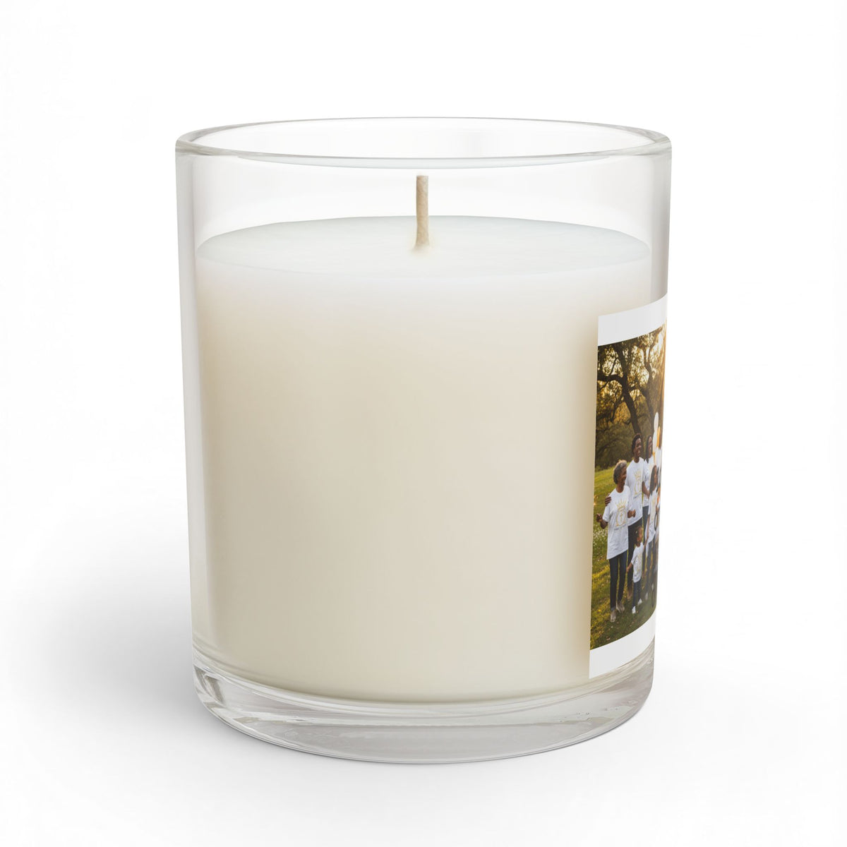 a personalized glass jar candle with creamy off- white wax and a single wick featuring a printed photo of  group of children on the side set against a plain white background 